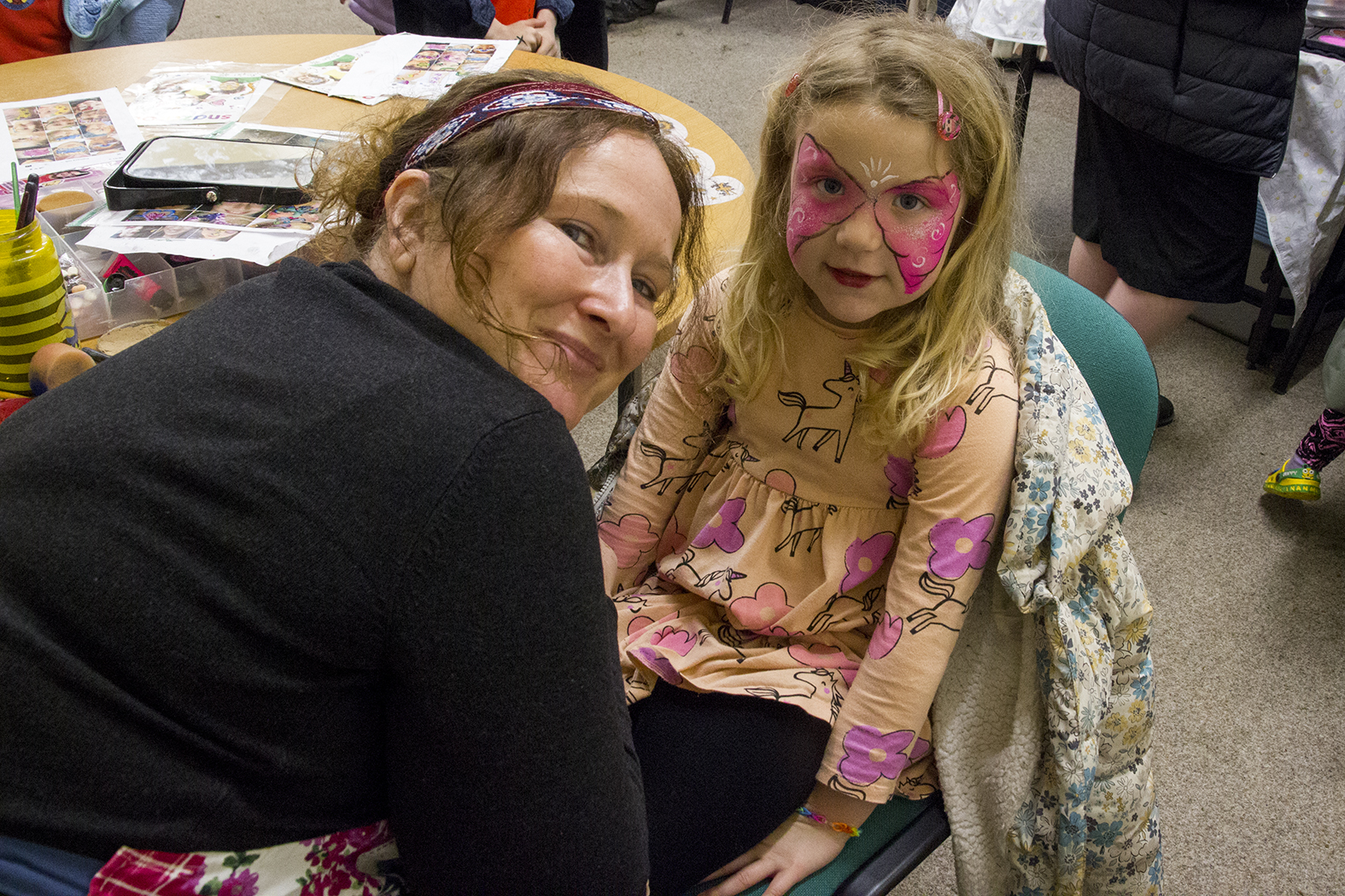 woman facepaints a butterfly on a little girl