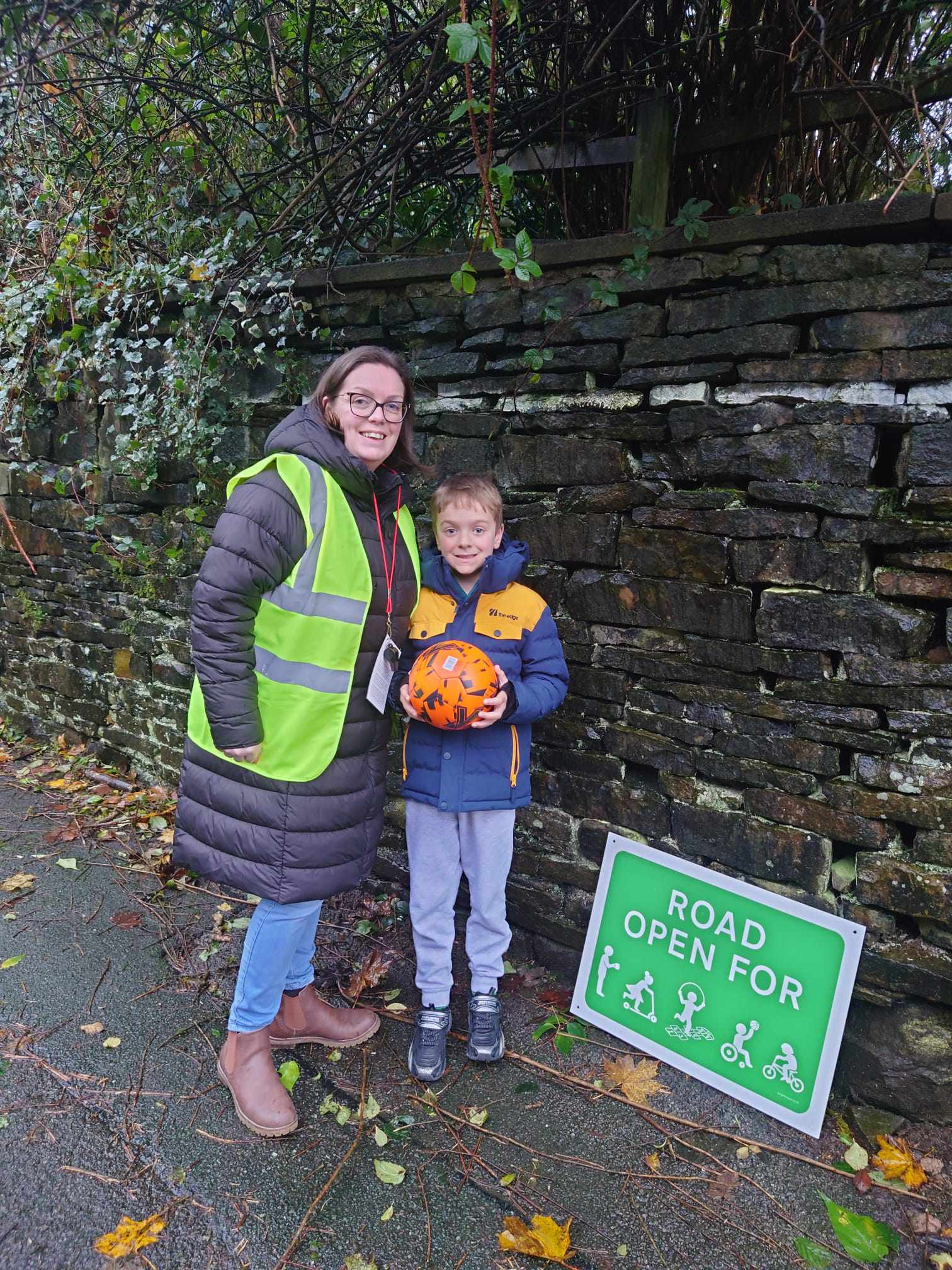 woman in high vis with small boy holding a football