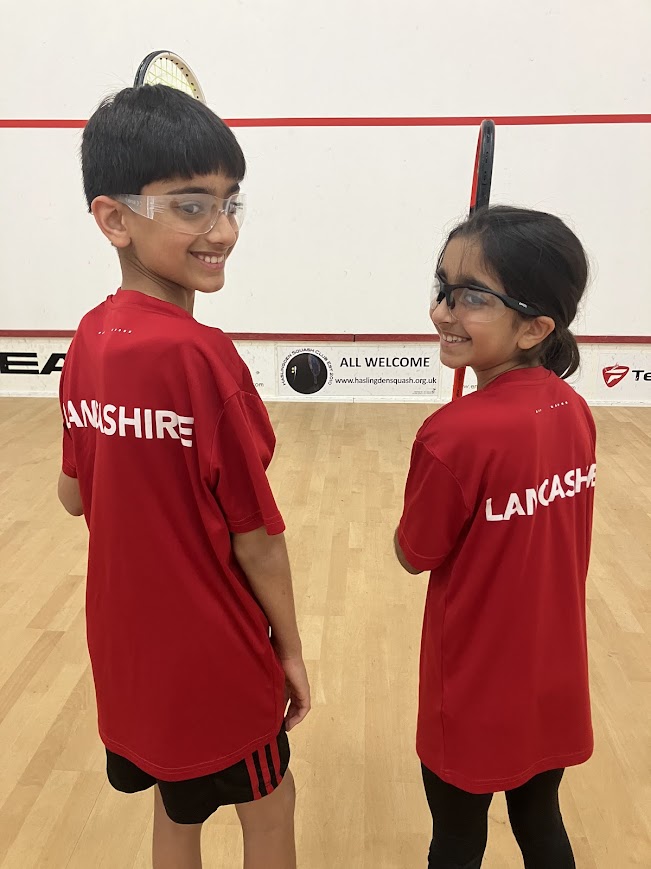 two kids with back to us in red shirts holding squash racketts